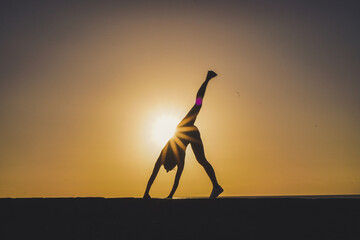 silhouette of a sportive athletic woman doing cartwheel on beach boardwalk during sunset 