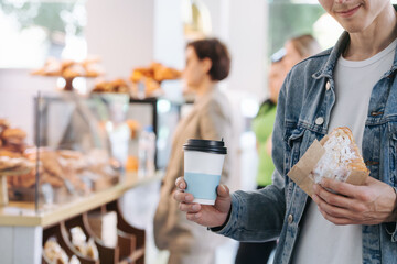 Bokeh image of a man in a jeans jacket holding coffee and croissant. Cropped