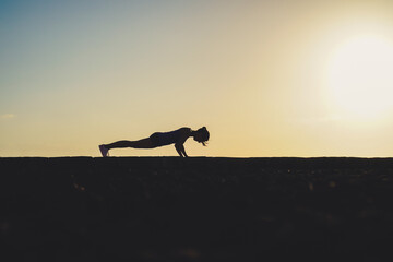 silhouette of a sportive athletic woman doing yoga on beach boardwalk during sunset 
