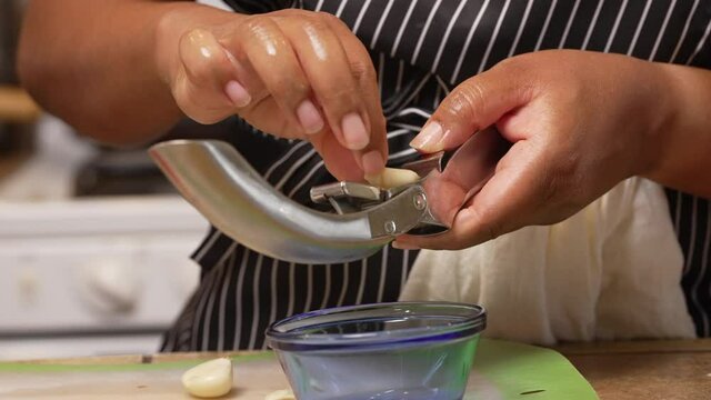 Squeezing cloves of garlic in a press for a special homemade dish - isolated slow motion