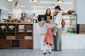 Woman paying for pastry in a bakery shop. Holding daughter by hand. - obrazy, fototapety, plakaty