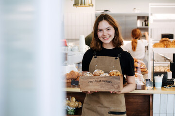 Friendly baker girl posing with a branded wooden box, filled with muffins - obrazy, fototapety, plakaty