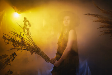 Young girl looking like witch having fun on Halloween in a dark room with yellow light and smoke. Teenager in Carnival and Halloween party