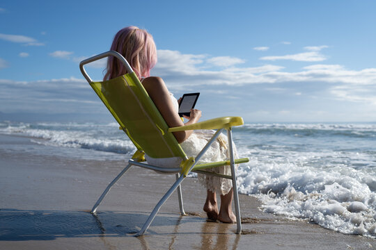 Anonymous woman reading on ebook tablet on beach