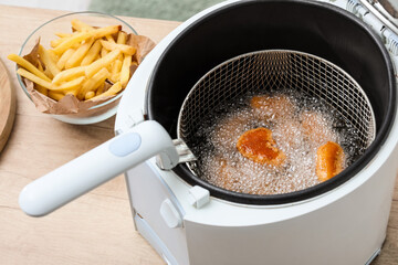 Modern deep fryer with nuggets and french fries on table in kitchen