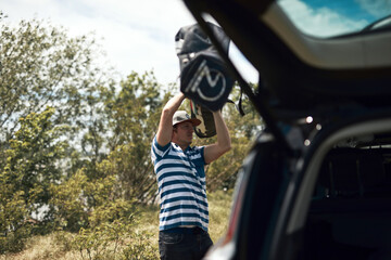 Windsurfer and camper packing and unpacking from a car in nature.