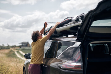Windsurfer and camper packing and unpacking from a car's roof rack in nature. © astrosystem