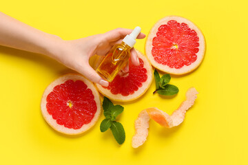 Female hand with bottle of essential oil and grapefruit slices on color background