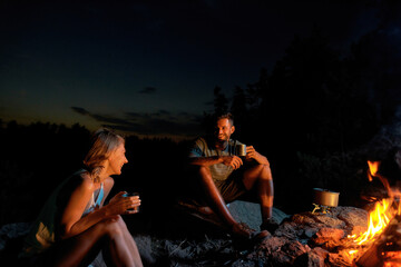 Cheerful young couple of tourists drinking tea or coffee, cooking a meal while relaxing together...
