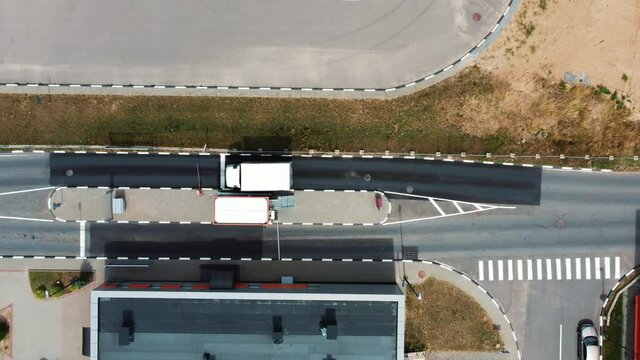 Aerial top view: Trucks stop at the border near the checkpoint for inspection of transported goods, checking documents or pay for travel. Barrier gate rising up and trucks driving away.