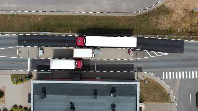 Aerial top view: Trucks stop at the border near the checkpoint for inspection of transported goods, checking documents or pay for travel. Barrier gate rising up and trucks driving away.