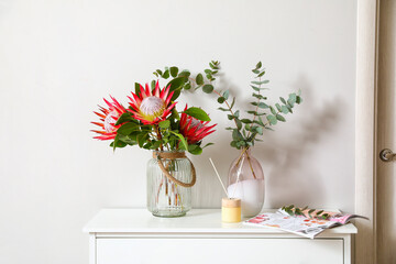 Chest of drawers with protea flowers near light wall