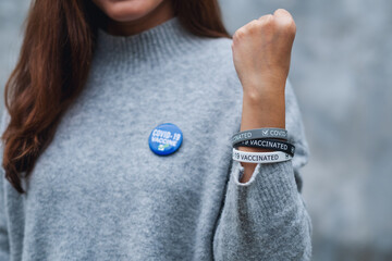 Closeup image of a young woman showing Covid-19 vaccinated wristband and brooch
