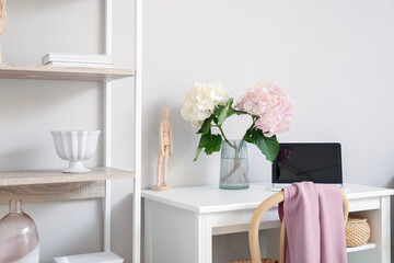 Stylish workplace with vase and hydrangea flowers near light wall