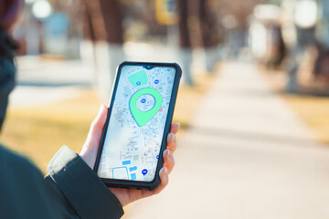 The concept of online navigators and modern technologies. A woman holds a cellphone with the online maps app open and looks at the marked location. Close up of hand. Blurred background