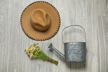 Watering can, hat and chamomile flowers on grey wooden background