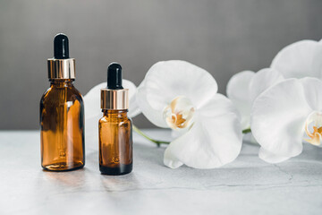 Serum or essential oil bottle mockup with orchid flowers in the background, natural beauty cosmetic skin products, home spa in a dropper bottle