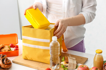 Woman packing meal into lunch box bag in kitchen