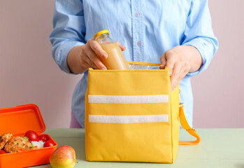 Woman packing meal into lunch box bag on color background