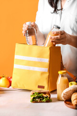 Woman packing meal into lunch box bag on color background
