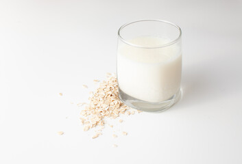 Sour milk in a glass next to raw oatmeal flakes on a white background.