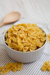Dry Organic Farfalle Pasta in a Bowl on a white wooden background, low angle view.