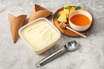 Container with tasty pineapple ice cream on light background