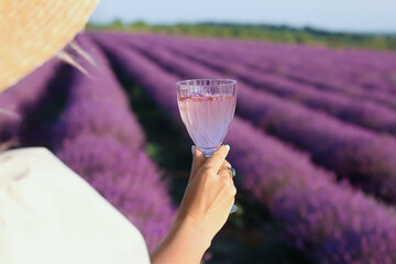 Beautiful young woman drinking wine in lavender field