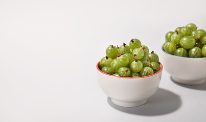 Bowls with fresh ripe gooseberry on light background
