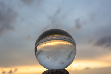 .view on the beach in beautiful sunset inside crystal ball placed on a timber by the sea. .Unconventional and beautiful natural views on the beach and sunset in a magic crystal ball. .