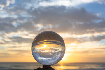 .view on the beach in beautiful sunset inside crystal ball placed on a timber by the sea. .Unconventional and beautiful natural views on the beach and sunset in a magic crystal ball. .