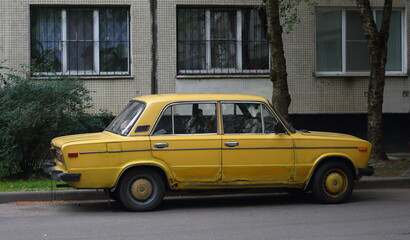 Fototapeta na wymiar An old yellow Soviet car in the courtyard of a residential building, Podvoysky Street, St. Petersburg, Russia, July 2021