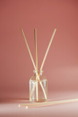 Liquid air freshener in a transparent glass vessel with wooden sticks on a delicate pink background. Aromatherapy spa bottles with aromatic oil and a stick. Traditional ethnic medicine.