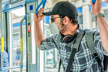 Young tourist with protective mask and backpack, traveling by tram, in the city.