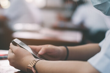Uniform students are test exam and study online by using smartphone and wearing protective facemask in classroom