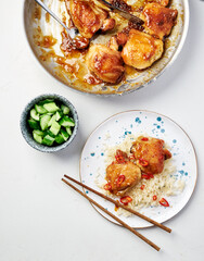 Vietnamese caramel chicken in a large bowl and 2 pieces of chicken lying on a plate. A bowl with cucumbers stands near them. Top view