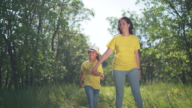 Happy family. Mom and daughter in forest park. People walk on grass. Happy team mom and daughter. Family is walk on grass in park. People walk along the tava in forest. Happy family concept