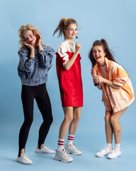 Pretty young women in retro 90s fashion style, outfits posing isolated over blue studio background....