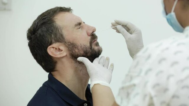 Coronavirus test - Close up of medical worker taking rapid nose swab for corona virus sample from young bearded man