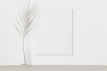 White canvas mockup on the wall with a palm leaf.