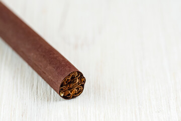 A single cigarette wrapped in brown paper on a white background close-up