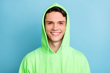 Photo of charming sweet young gentleman wear green sweatshirt hood smiling isolated blue color...
