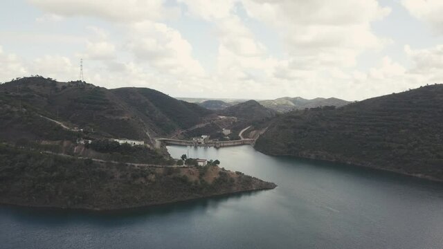 Aerial flyover natural lake in Funcho de Diante surrounded by hills with road during sunset.
