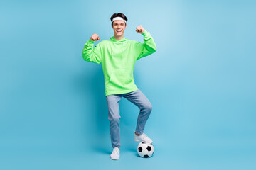 Fototapeta na wymiar Photo of cool confident young guy dressed green hoodie playing football showing strength smiling isolated blue color background