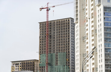 Fototapeta na wymiar Finished residential building, unfinished residential buildings and construction cranes against clear blue sky. Housing construction site, apartment block with scaffolding