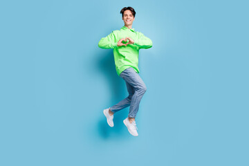 Fototapeta na wymiar Photo of sweet charming young gentleman wear green sweatshirt smiling jumping showing fingers heart isolated blue color background