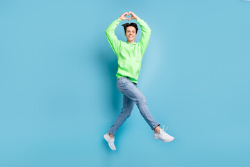 Photo of romantic boyfriend jump fingers show heart symbol wear green hoodie jeans shoes isolated blue color background