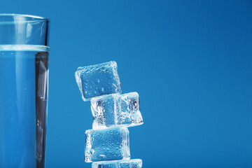 A glass of refreshing water and a tower of ice cubes on a blue background