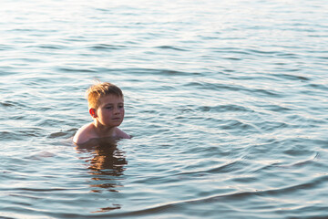 Cute young boy enjoy having fun at lake or river beach water on warm sunset evening time outdoors.