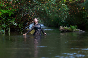 woman in a dark lace dress splashes in the river